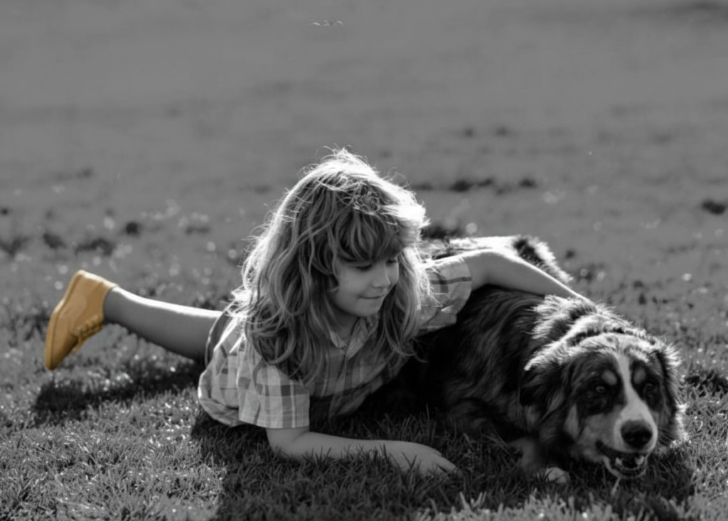 Une fillette allongée dans l’herbe auprès de son chien, en noir et blanc