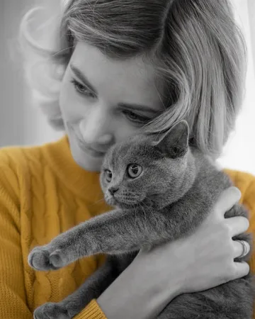Une femme tient son chat gris contre elle, dans un pull jaune