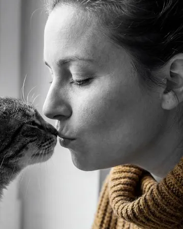 Une femme embrasse son chat près d’une fenêtre