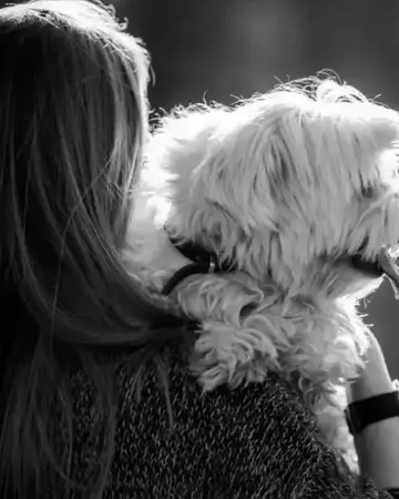 Une femme tient contre elle son petit chien blanc, en noir et blanc