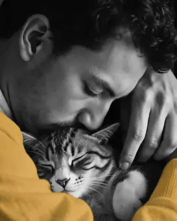 Un homme serre son chat contre lui, en pull jaune